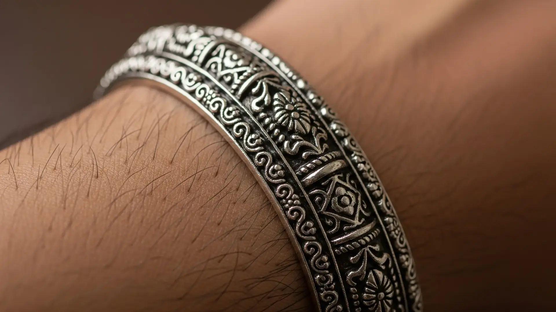A close-up of a man's wrist wearing an intricately designed oxidized silver Kada style Rakhi, showcasing its regal, rustic, and reusable appeal for brothers.